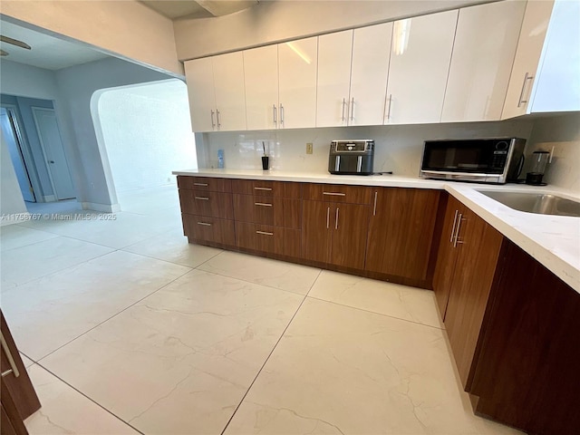 kitchen with white cabinetry, stainless steel microwave, arched walkways, light countertops, and decorative backsplash