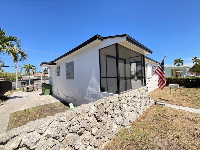 view of side of property with a sunroom, stucco siding, a patio, and fence