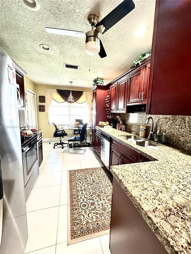 kitchen with reddish brown cabinets, light tile patterned floors, decorative backsplash, appliances with stainless steel finishes, and a sink