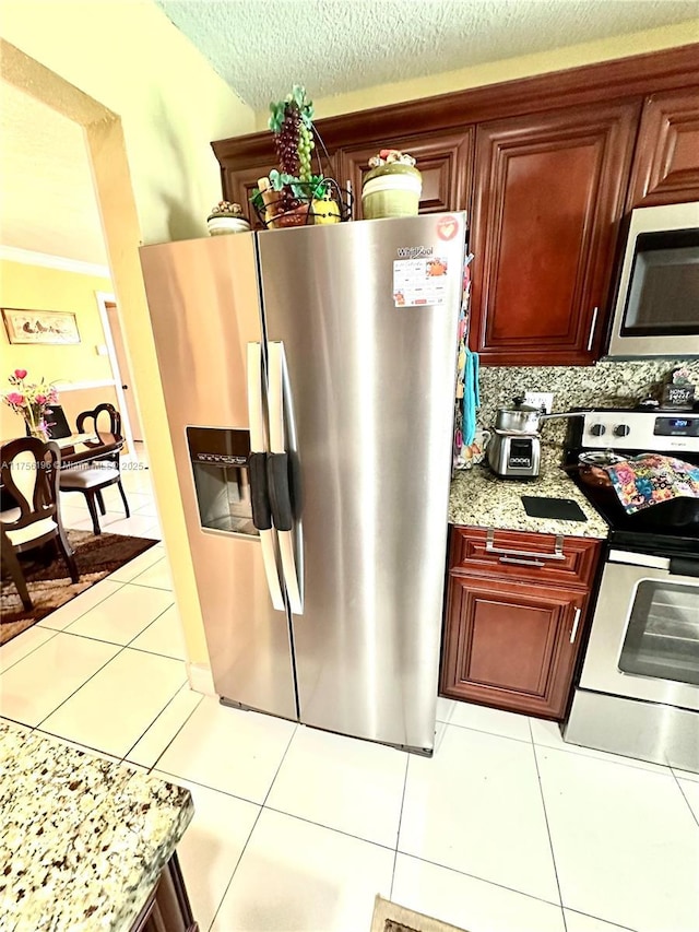 kitchen featuring reddish brown cabinets, light tile patterned floors, tasteful backsplash, appliances with stainless steel finishes, and a textured ceiling