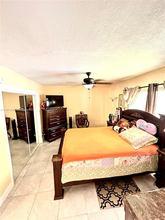 bedroom featuring a textured ceiling, a closet, light tile patterned flooring, and a ceiling fan