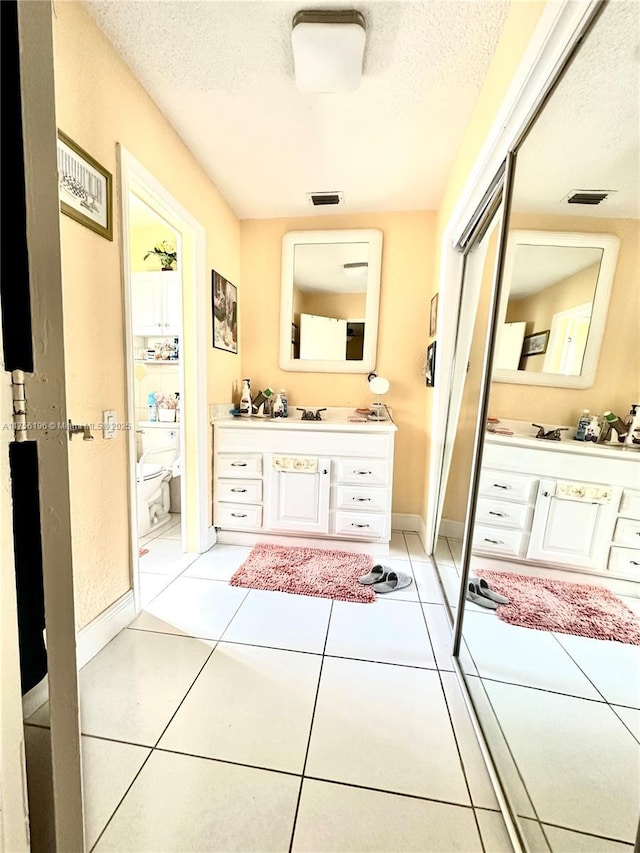 bathroom featuring a textured ceiling, toilet, vanity, visible vents, and tile patterned floors