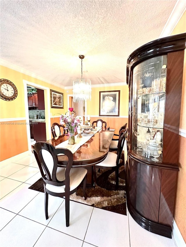 tiled dining area with a textured ceiling, an inviting chandelier, a sink, and crown molding