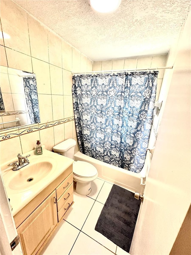 bathroom with tile patterned floors, shower / bathtub combination with curtain, a textured ceiling, vanity, and tile walls