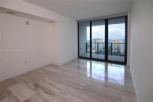 spare room featuring a view of city, a wall of windows, and baseboards