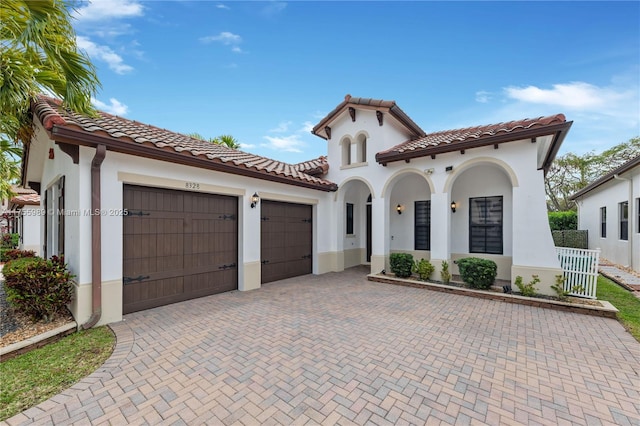 mediterranean / spanish house with a tiled roof, decorative driveway, a garage, and stucco siding