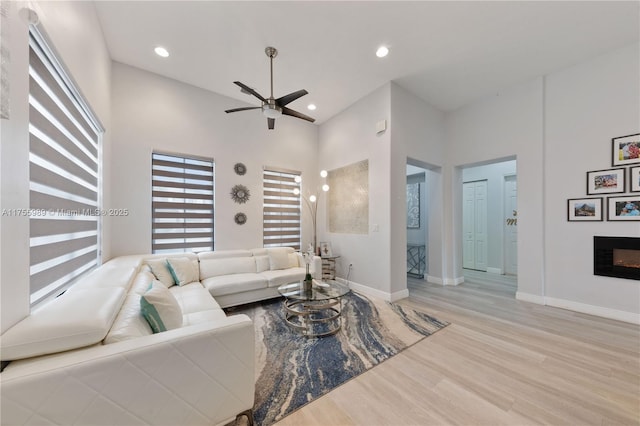 living area featuring a fireplace, a high ceiling, baseboards, and wood finished floors