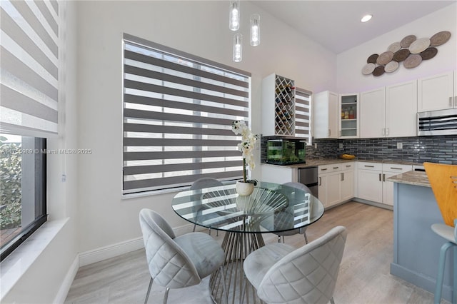 kitchen with light wood finished floors, glass insert cabinets, white cabinetry, stainless steel microwave, and tasteful backsplash