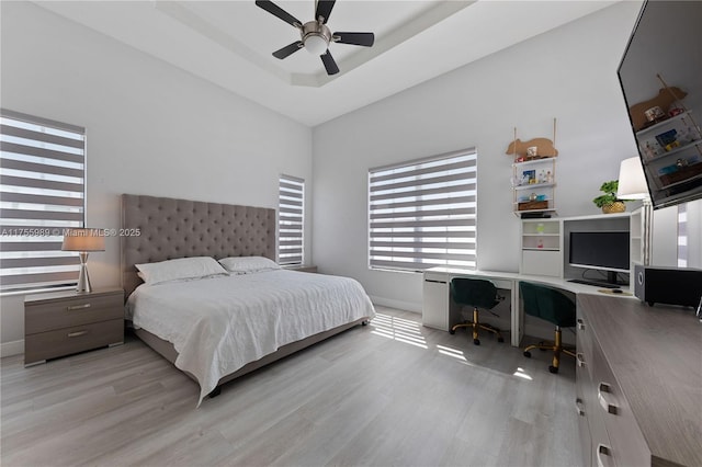 bedroom featuring ceiling fan, baseboards, a tray ceiling, and wood finished floors