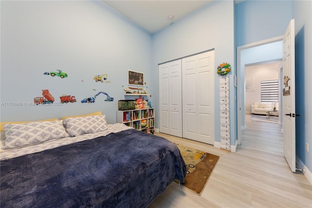 bedroom with a closet, baseboards, light wood-style floors, and a towering ceiling