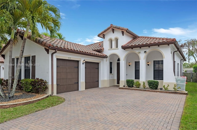 mediterranean / spanish-style home featuring decorative driveway, a tile roof, an attached garage, and stucco siding