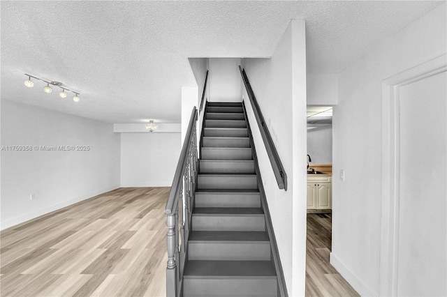 staircase with a textured ceiling, baseboards, and wood finished floors