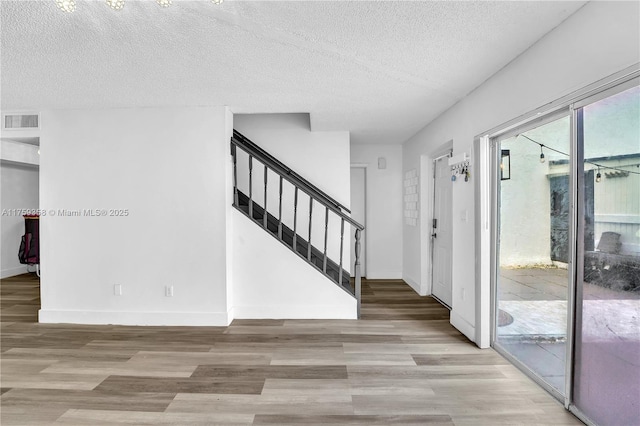 foyer featuring baseboards, visible vents, stairway, a textured ceiling, and light wood-type flooring