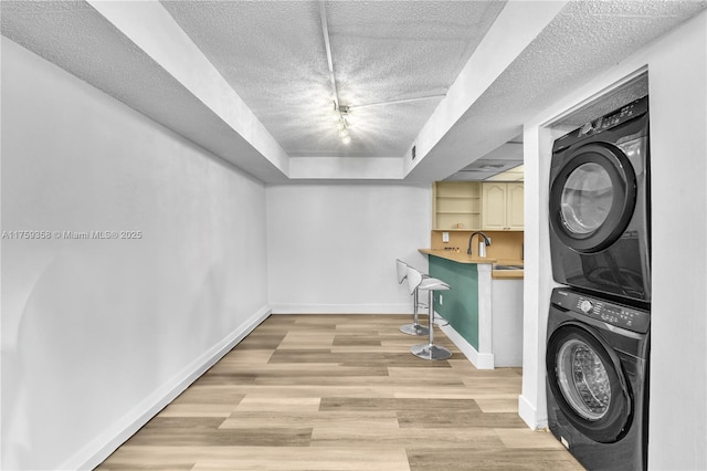 laundry area with a textured ceiling, laundry area, baseboards, light wood finished floors, and stacked washer and clothes dryer