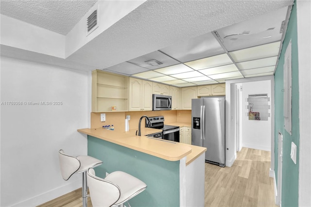 kitchen featuring stainless steel appliances, visible vents, light countertops, light wood-style floors, and a peninsula