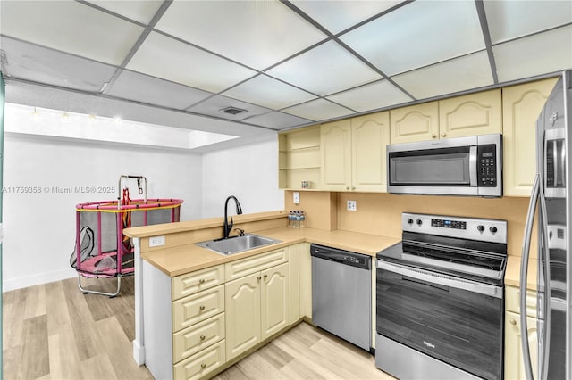 kitchen featuring cream cabinets, a peninsula, a sink, light countertops, and appliances with stainless steel finishes