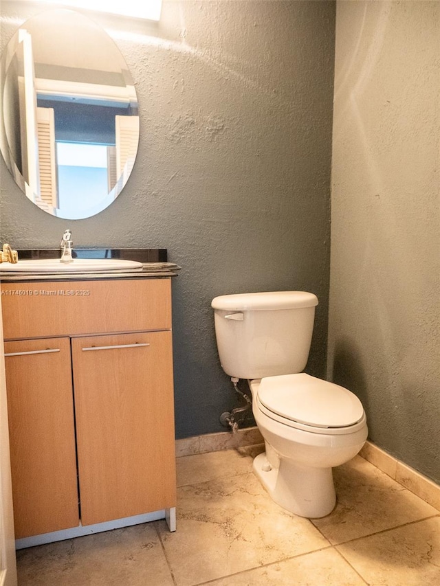 half bathroom featuring baseboards, a textured wall, vanity, and toilet