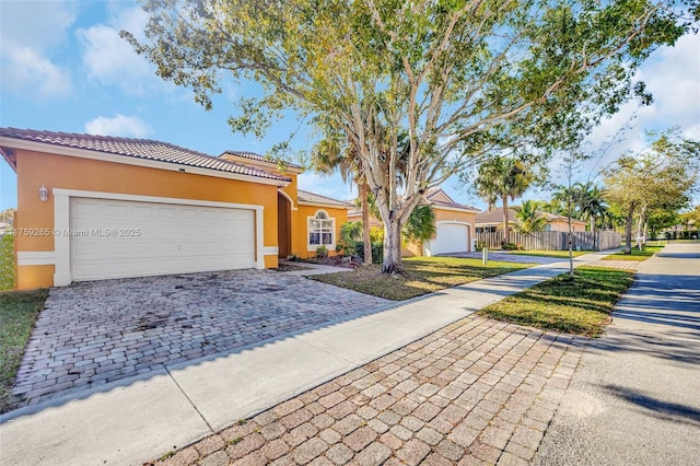 view of front of home featuring stucco siding, decorative driveway, fence, an attached garage, and a tiled roof