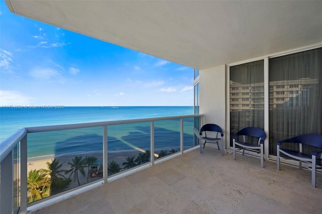 balcony with a water view, a sunroom, and a view of the beach