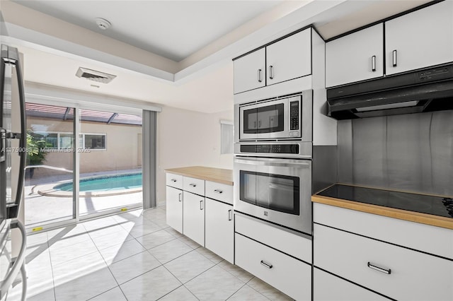 kitchen with light tile patterned floors, stainless steel appliances, white cabinetry, and under cabinet range hood