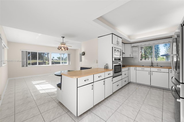 kitchen with light tile patterned floors, butcher block counters, appliances with stainless steel finishes, a sink, and a peninsula