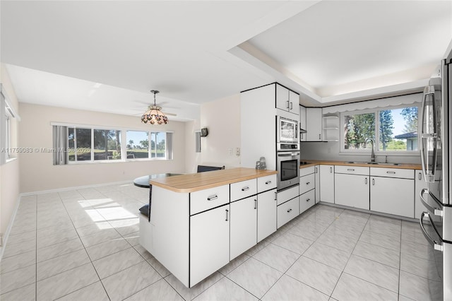 kitchen with appliances with stainless steel finishes, a sink, a peninsula, wooden counters, and light tile patterned floors