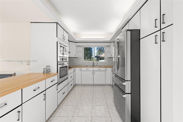 kitchen with light tile patterned floors, a raised ceiling, appliances with stainless steel finishes, white cabinetry, and a sink