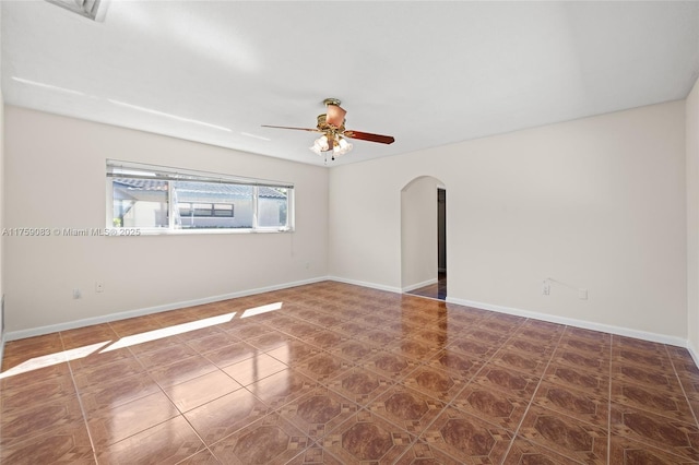 tiled spare room featuring arched walkways, ceiling fan, and baseboards