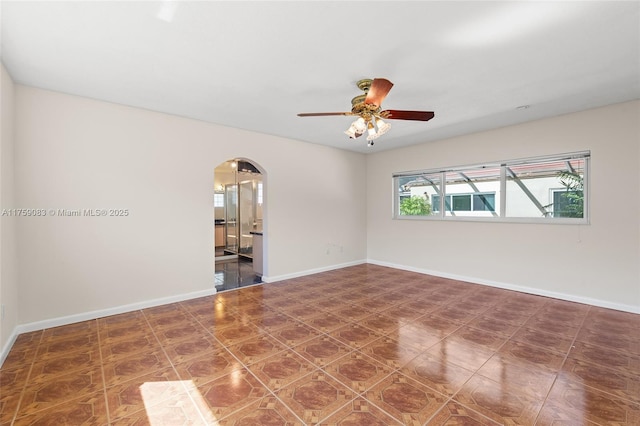 spare room featuring arched walkways, ceiling fan, and baseboards