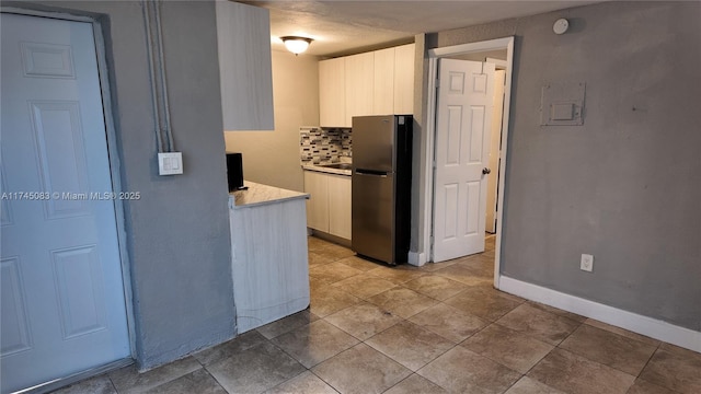 kitchen with baseboards, white cabinets, freestanding refrigerator, light countertops, and backsplash