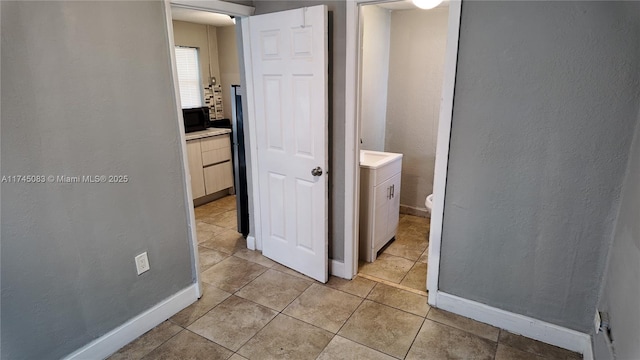 hall featuring light tile patterned floors, a textured wall, and baseboards