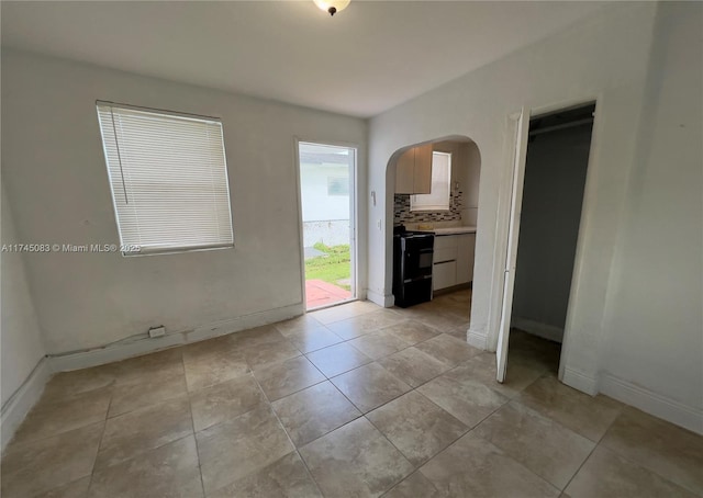 empty room featuring light tile patterned floors, baseboards, and arched walkways