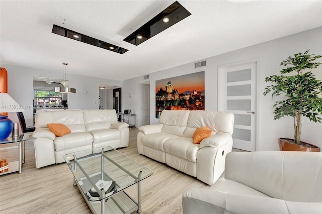 living room featuring visible vents, a textured ceiling, and light wood finished floors