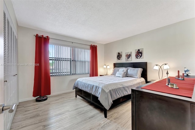 bedroom with light wood finished floors, baseboards, and a textured ceiling