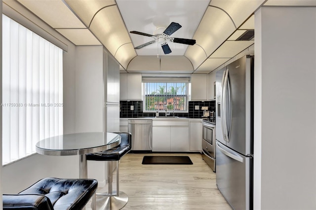 kitchen featuring visible vents, a ceiling fan, appliances with stainless steel finishes, light wood-type flooring, and backsplash