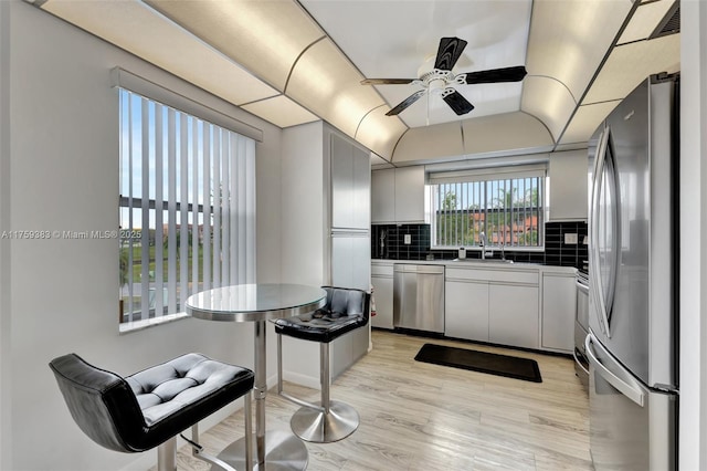 kitchen with lofted ceiling, appliances with stainless steel finishes, light wood finished floors, dark countertops, and tasteful backsplash