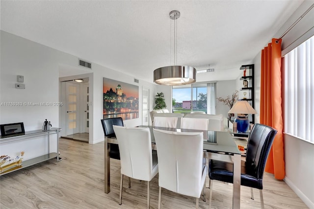 dining space featuring baseboards, visible vents, a textured ceiling, and light wood finished floors