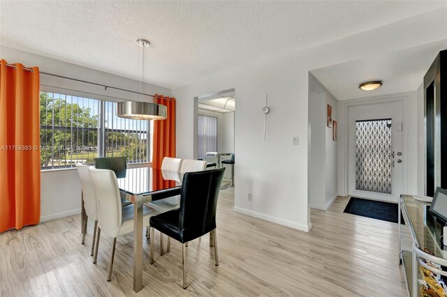 dining space with a textured ceiling, light wood finished floors, and baseboards