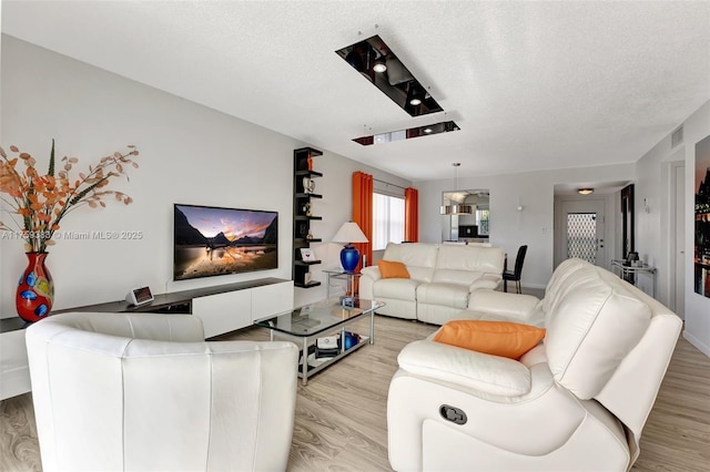 living room featuring a textured ceiling, light wood finished floors, and visible vents