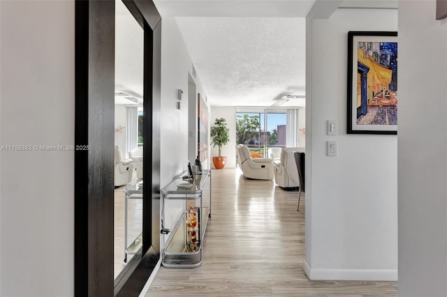 hallway featuring a textured ceiling, light wood finished floors, and baseboards