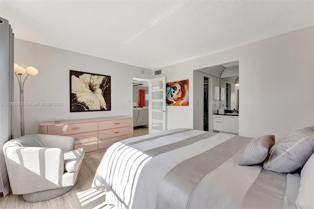 bedroom with visible vents, ensuite bath, and light wood finished floors