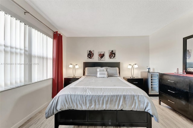 bedroom featuring light wood-type flooring, wine cooler, baseboards, and a textured ceiling