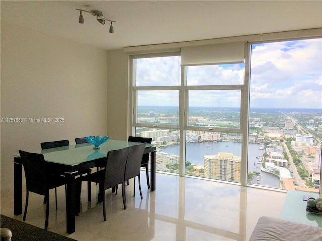 dining room with a water view, a view of city, expansive windows, and track lighting