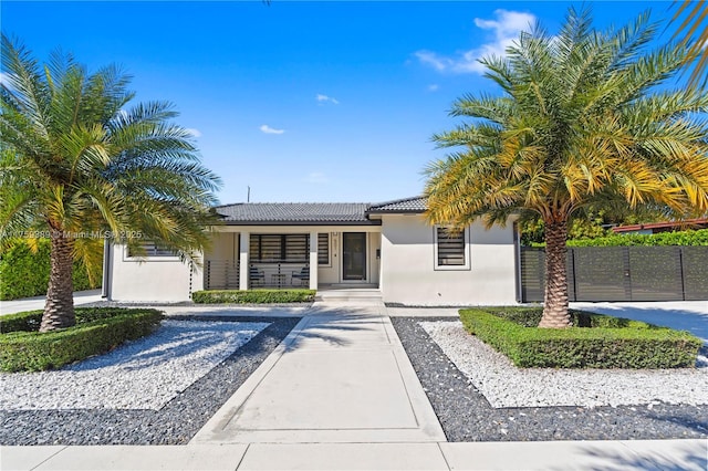 ranch-style home featuring covered porch, a tiled roof, fence, and stucco siding