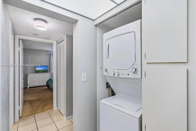 laundry room featuring stacked washer / drying machine, laundry area, a textured ceiling, and light tile patterned floors