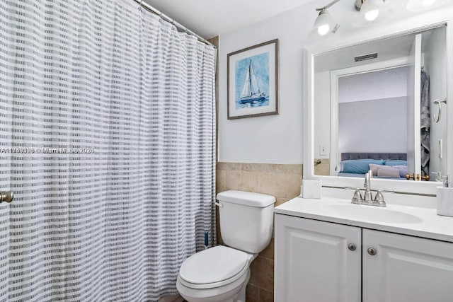 ensuite bathroom featuring toilet, a wainscoted wall, ensuite bathroom, vanity, and tile walls