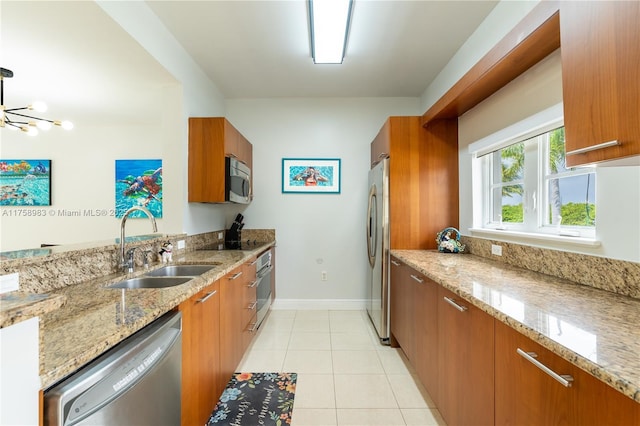 kitchen featuring brown cabinetry, appliances with stainless steel finishes, light stone countertops, a sink, and light tile patterned flooring