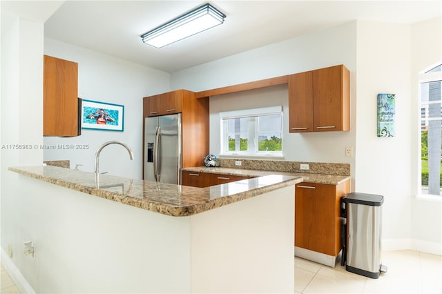 kitchen with brown cabinetry, stainless steel fridge, and light stone countertops