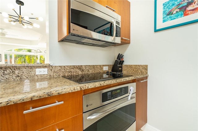 kitchen with pendant lighting, stainless steel appliances, brown cabinetry, and light stone countertops