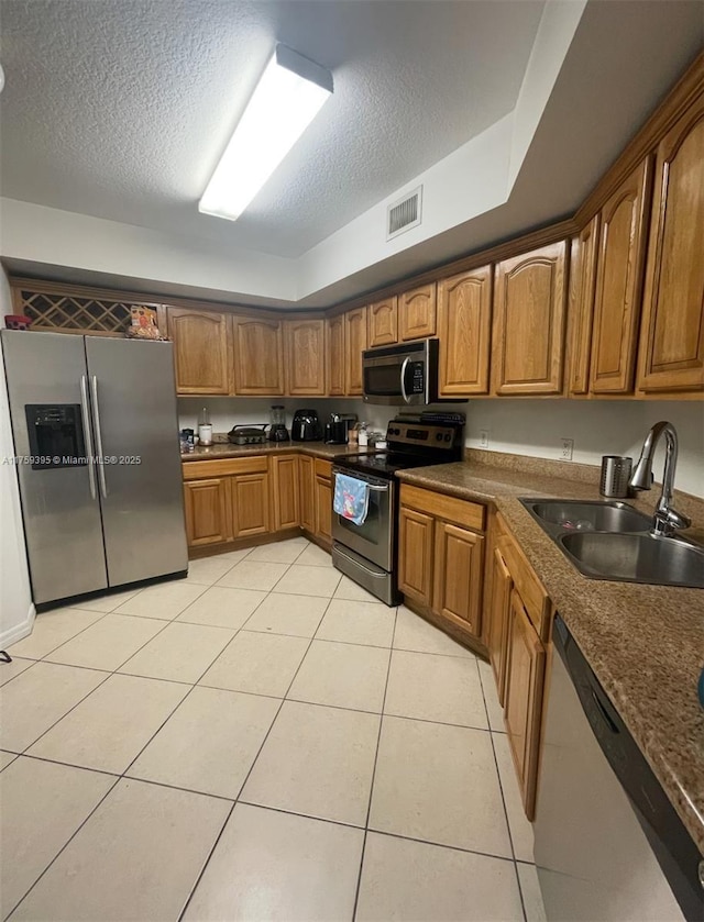 kitchen with light tile patterned floors, visible vents, appliances with stainless steel finishes, brown cabinets, and a sink